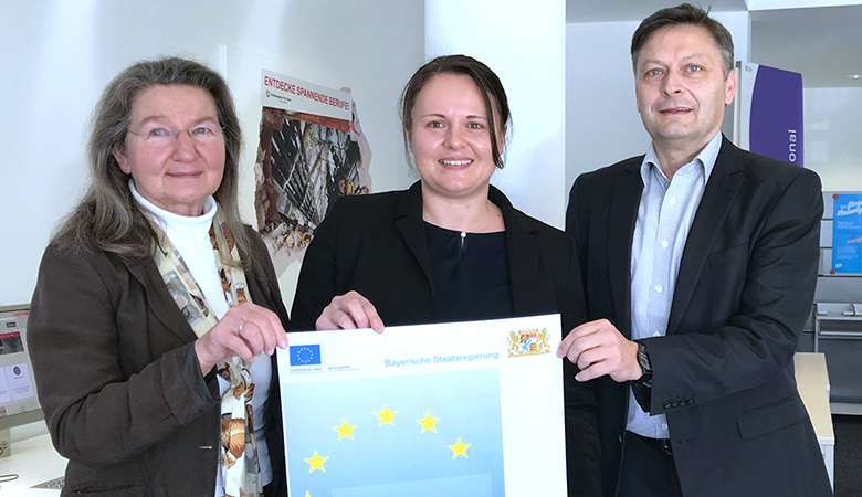 Zwei Frauen und ein Mann halten ein Plakat des ESF+ und dem Bayerischen Staatsministerium in die Kamera.